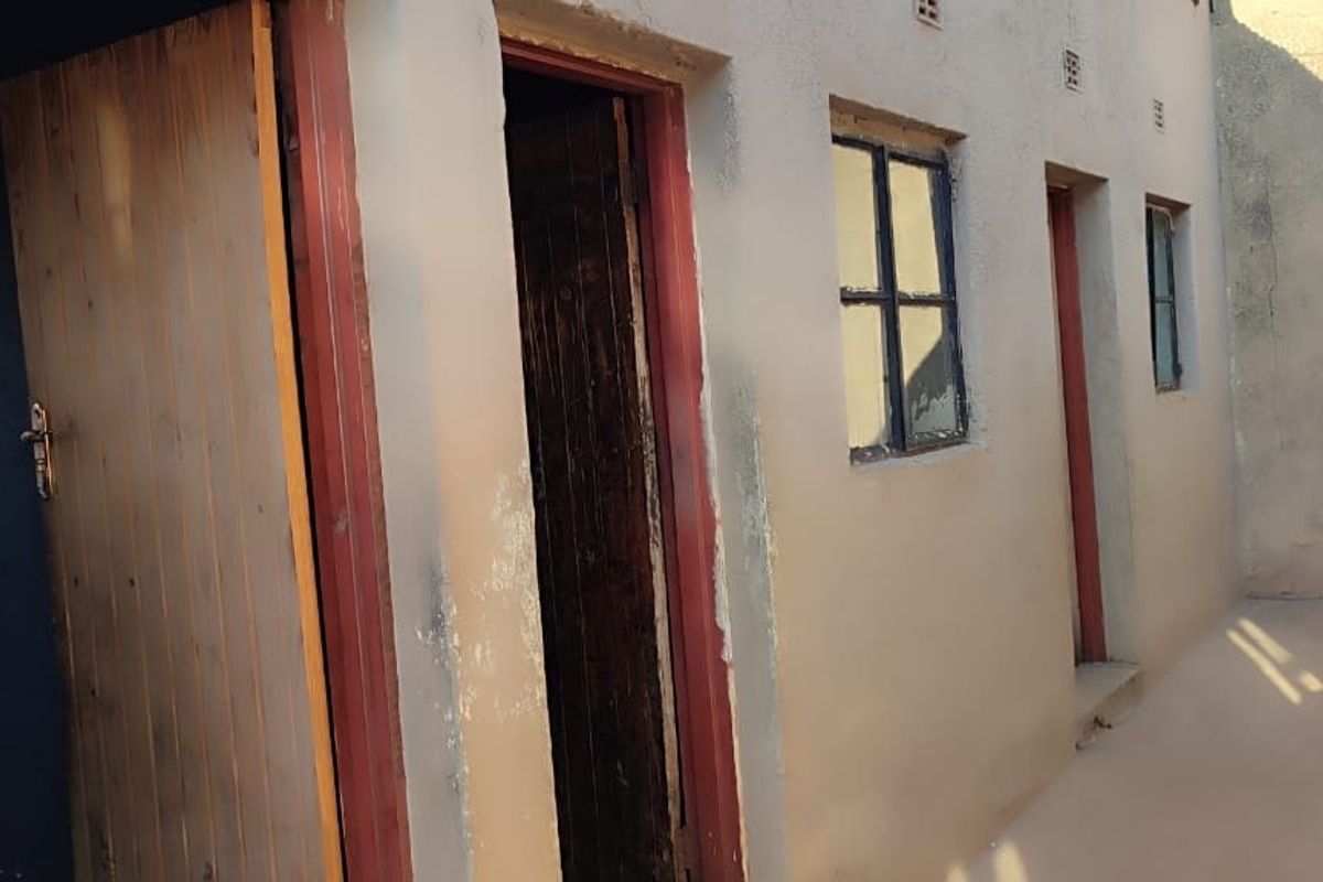 Rear exterior view of the property showing plastered masonry walls, steel-framed windows, and multiple timber access doors.