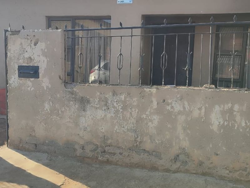 Front elevation of the property featuring a weathered boundary wall, wrought iron fencing, and a gated entrance.