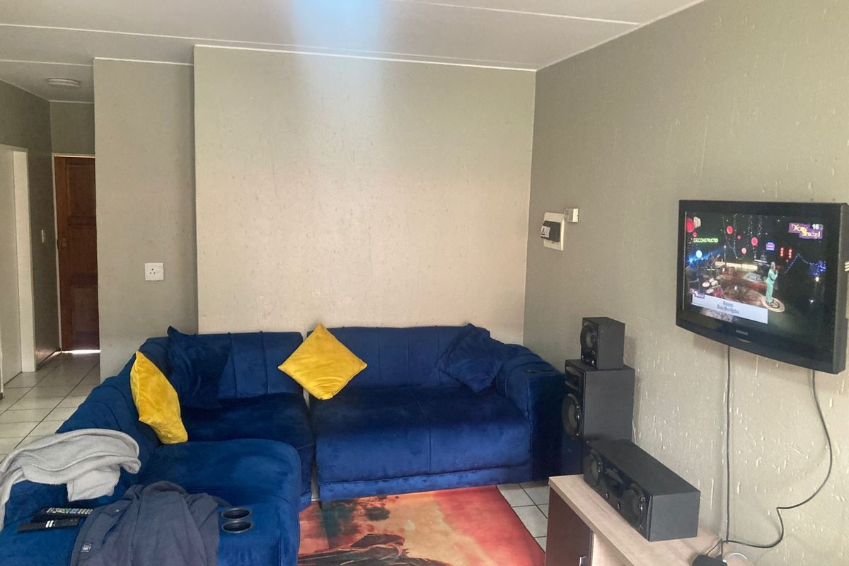 A living room area featuring tiled flooring and wall-mounted television setup, requiring cosmetic updates to the wall finishes.