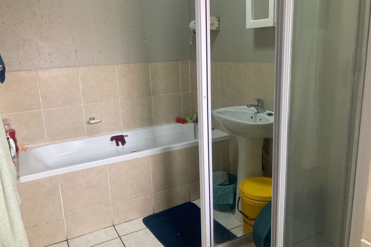 A functional bathroom featuring a bathtub, pedestal basin, and separate shower enclosure with tiled finishes, requiring cosmetic updates to improve its overall condition.