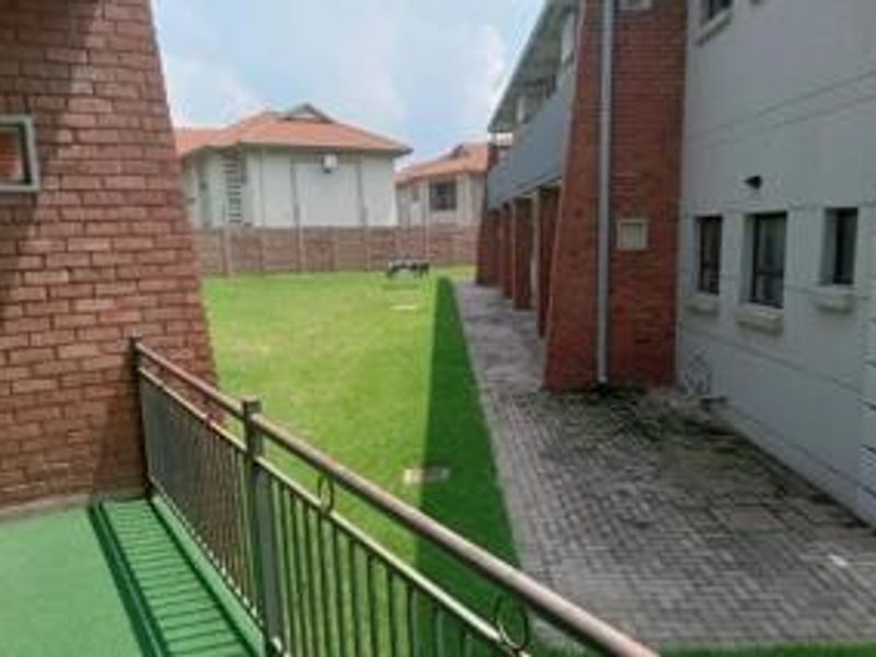 Rear exterior view showing a paved walkway, metal railing, and a shared lawn area between residential buildings.