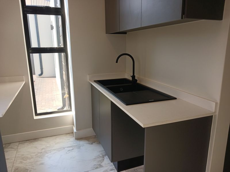 A modern, minimalist scullery featuring sleek dark cabinetry, a contrasting stone countertop, and a contemporary black sink and tap fixture.