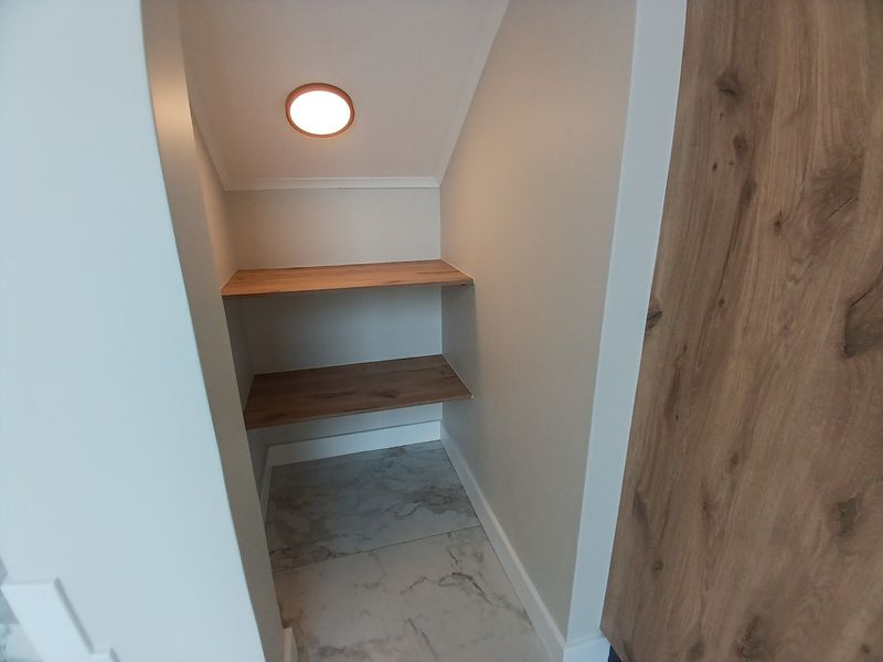 A clean, modern utility storage nook featuring built-in wooden shelving, marble-look floor tiles, and integrated recessed lighting.
