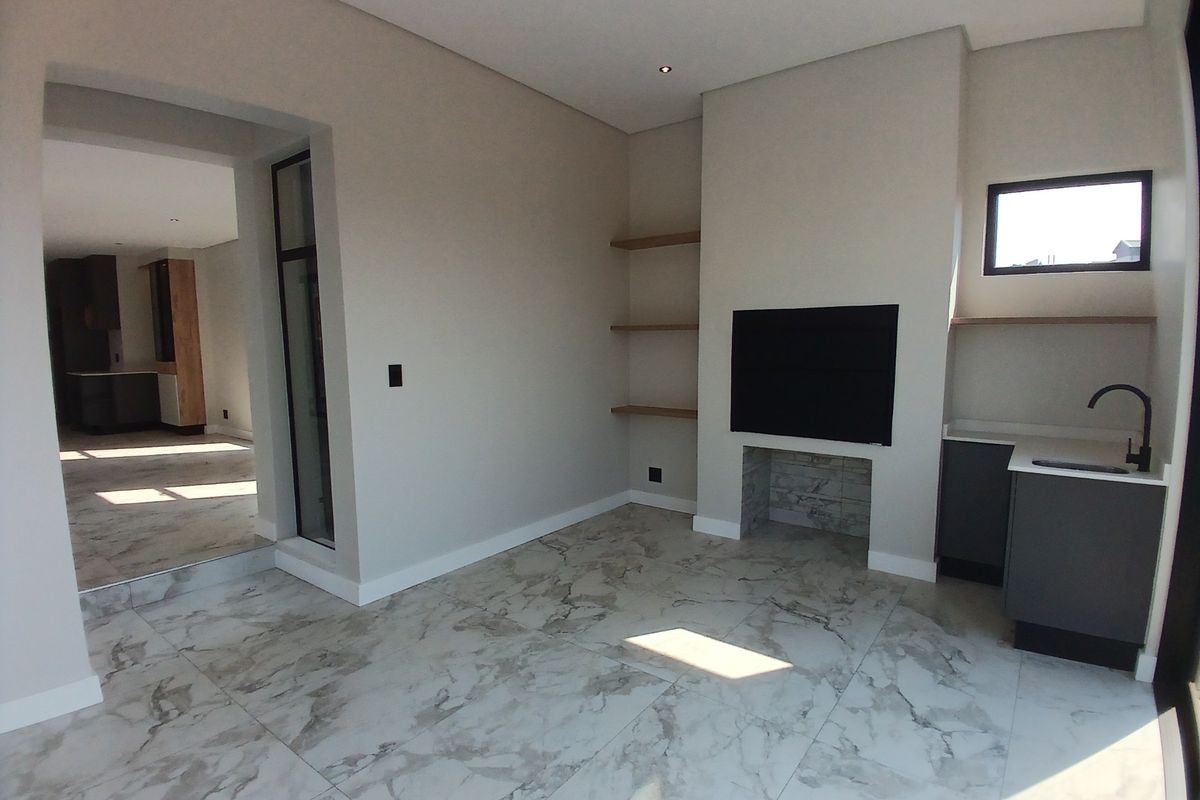 Modern living area featuring marble-look floor tiles, built-in fireplace, floating shelves, and a convenient kitchenette corner with sink and cabinetry.