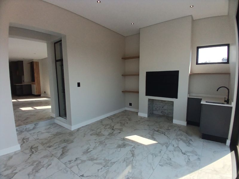 Modern living area featuring marble-look floor tiles, built-in fireplace, floating shelves, and a convenient kitchenette corner with sink and cabinetry.