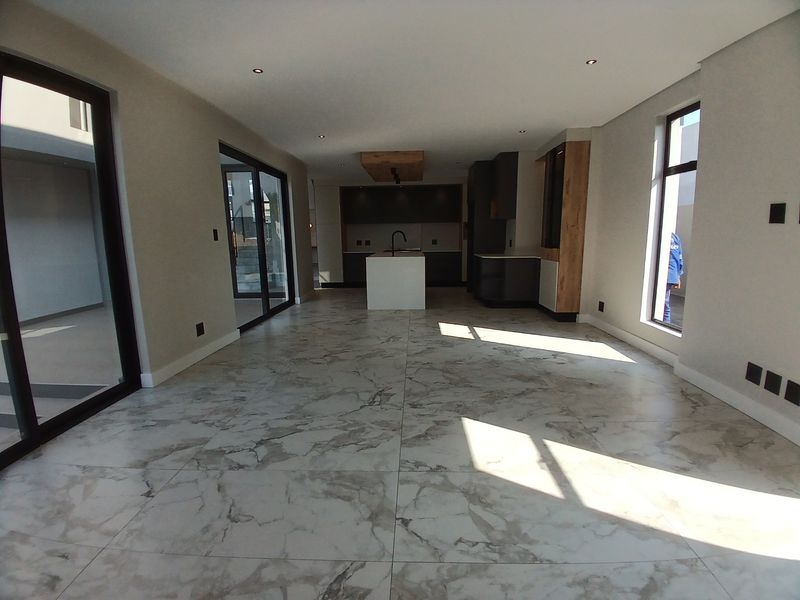 Spacious open-plan living and kitchen area featuring modern marble-look floor tiles, sleek cabinetry, a central kitchen island, and large glass sliding doors.