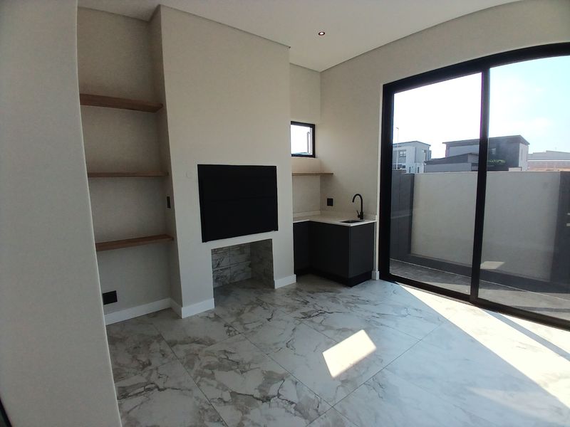 Modern covered patio featuring a built-in braai, stone prep area with sink, floating shelving, and large sliding doors opening to the exterior.