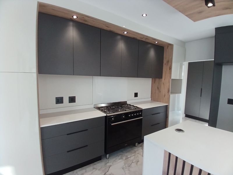 Modern kitchen featuring dark matte cabinetry, stone countertops, a gas range, and a central island with integrated lighting and marble-look flooring.
