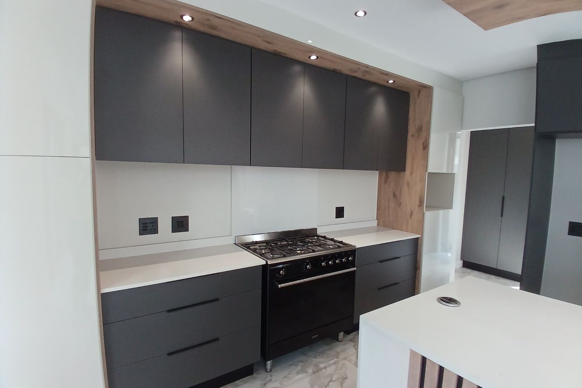 Modern kitchen featuring dark matte cabinetry, stone countertops, a gas range, and a central island with integrated lighting and marble-look flooring.