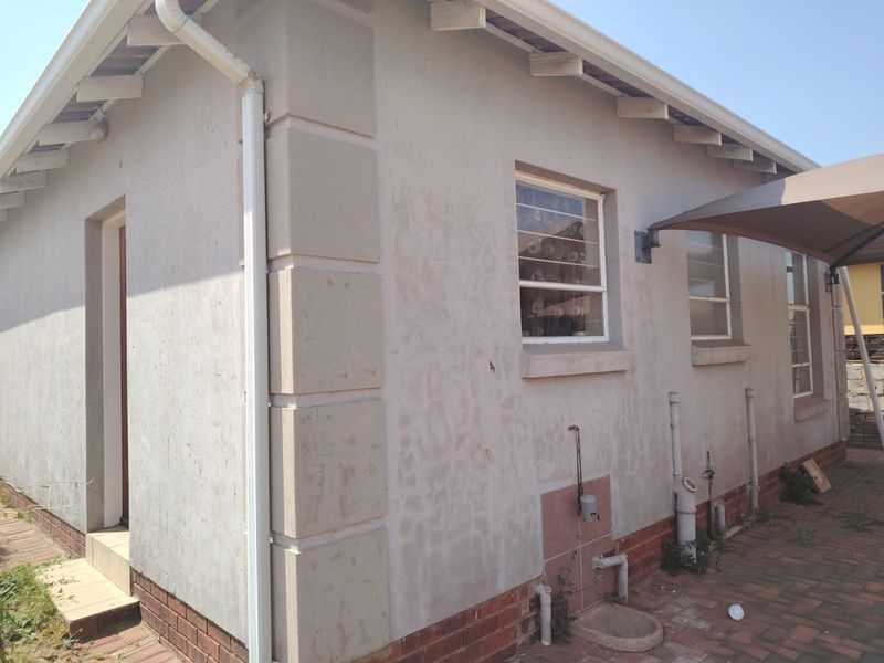 Rear exterior view of the property featuring brick paving, external plumbing fixtures, and a shade sail structure over the paved area.