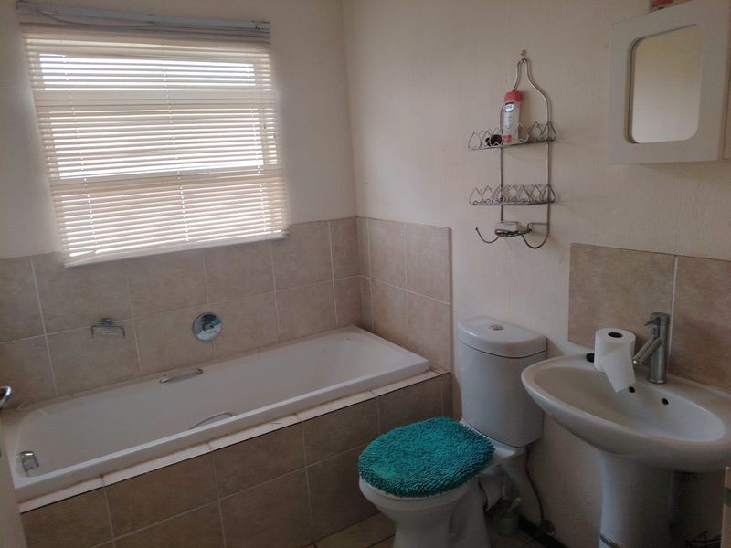 A functional bathroom featuring a built-in bathtub, pedestal washbasin, and close-coupled toilet with neutral wall tiling.