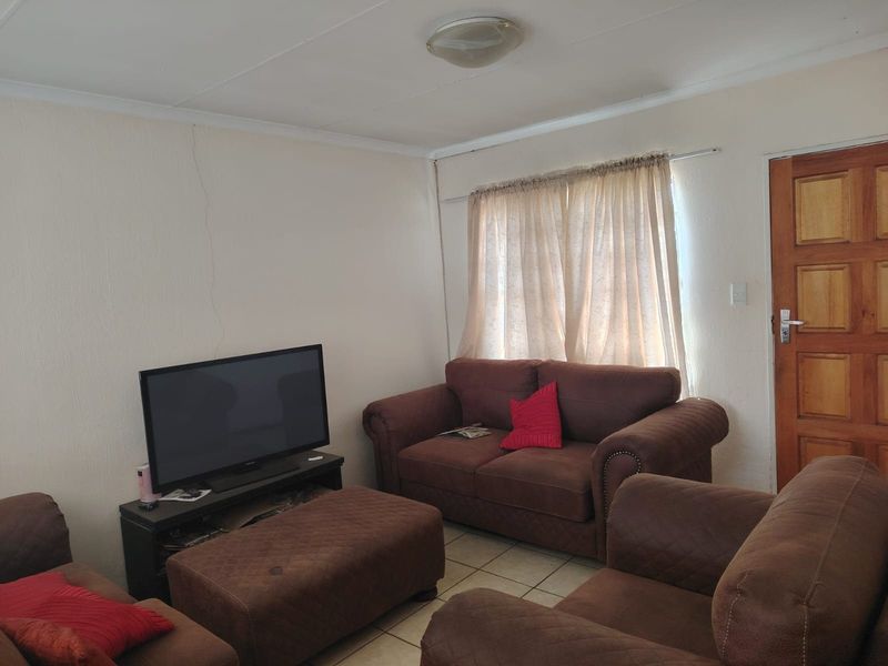 A living room featuring tiled flooring and a timber panel door, showing a visible vertical crack on the wall requiring maintenance.