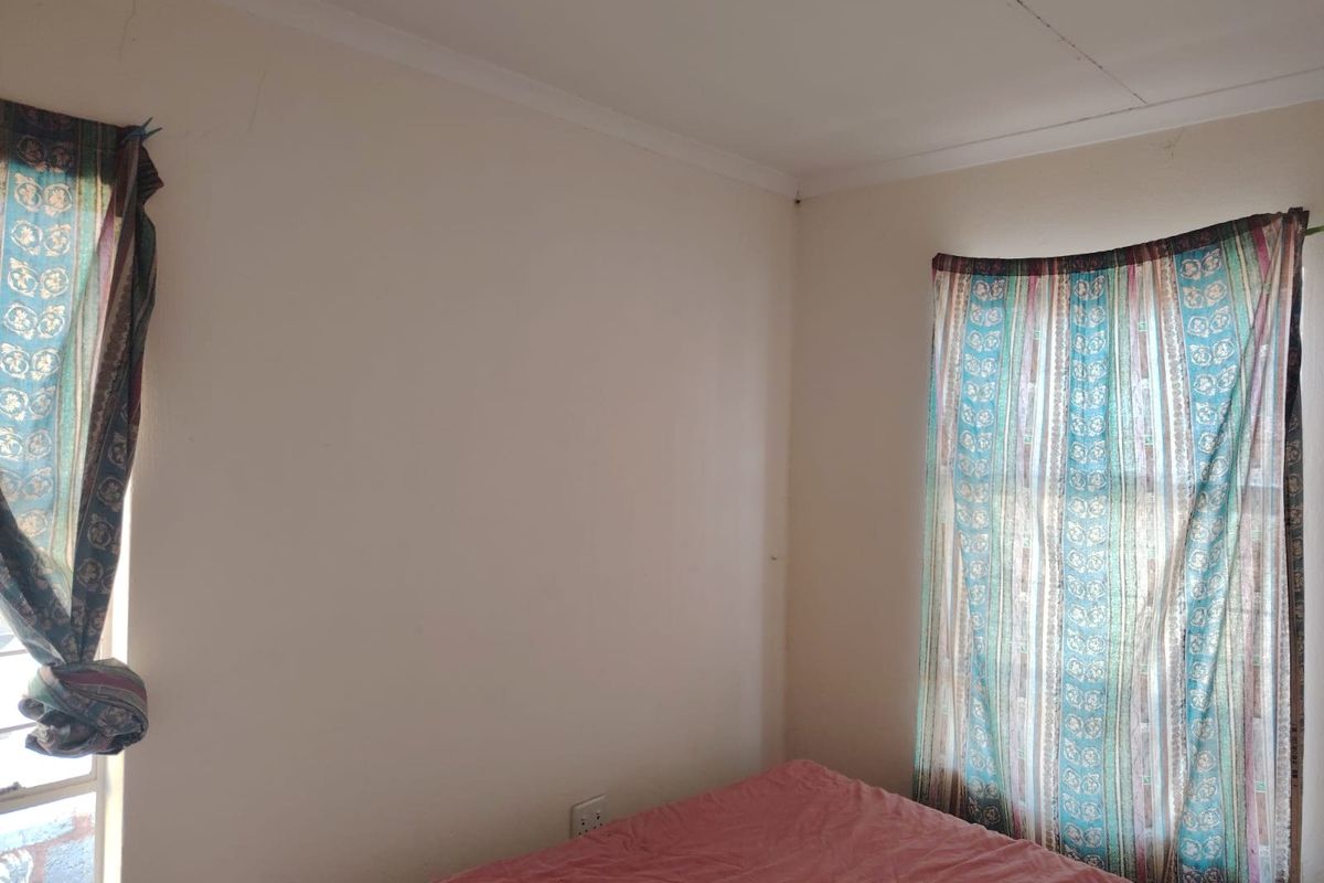 A bedroom corner featuring plain walls with visible hairline cracks and standard window treatments.