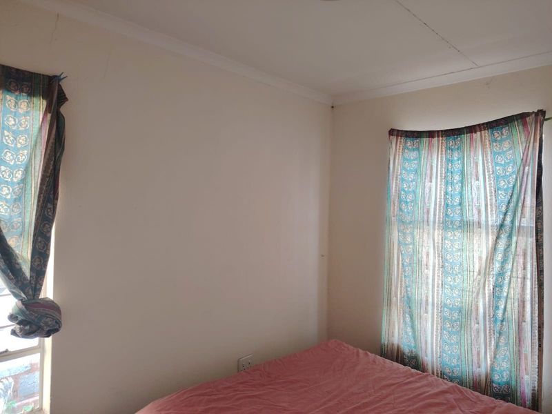 A bedroom corner featuring plain walls with visible hairline cracks and standard window treatments.