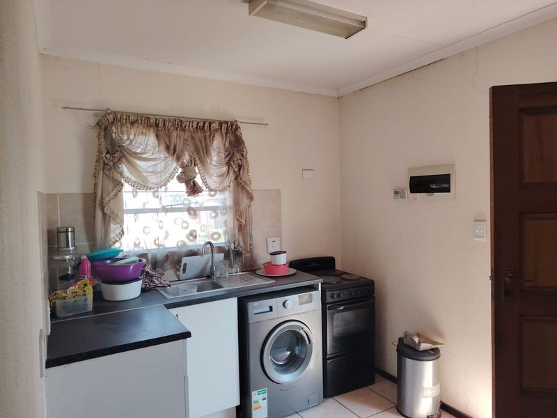 A compact kitchen area featuring a stainless steel sink, tiled splashback, and built-in cabinetry, showing signs of wear and requiring cosmetic updates.