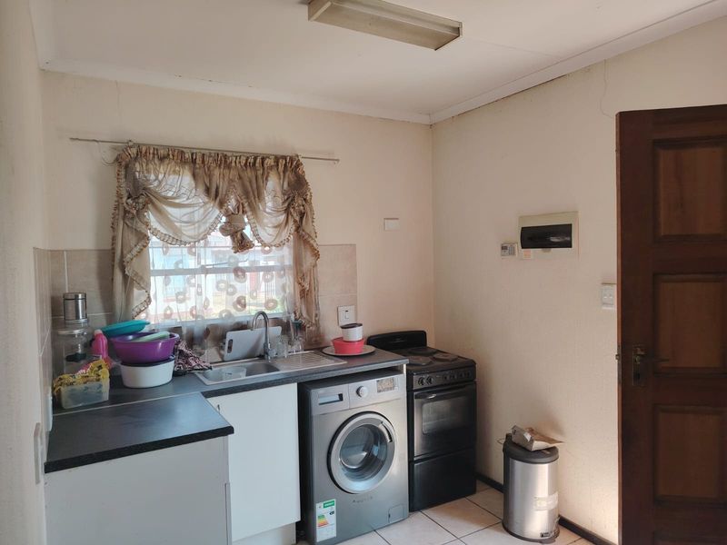 A compact kitchen featuring laminate countertops, a stainless steel sink, and space for a washing machine and freestanding stove.