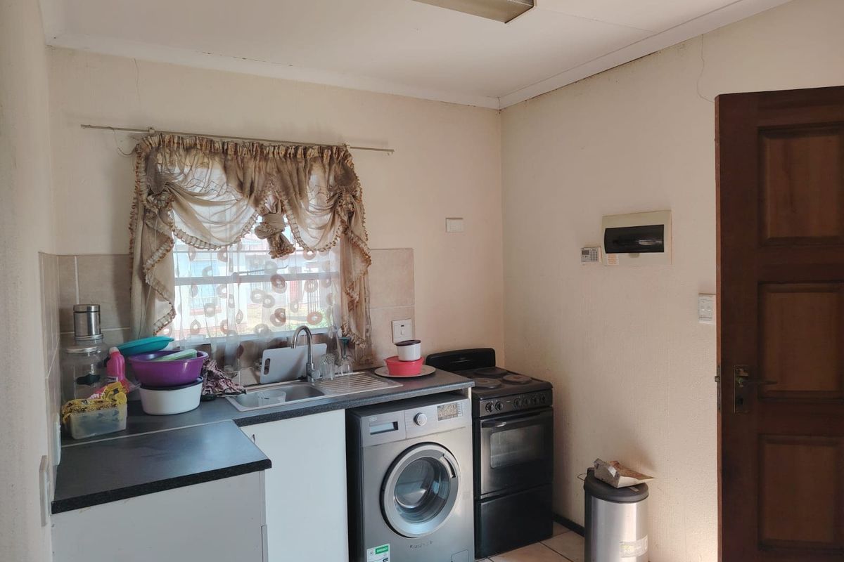A compact kitchen featuring laminate countertops, a stainless steel sink, and space for a washing machine and freestanding stove.