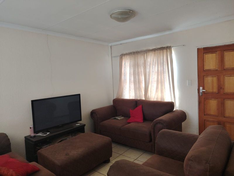 A living room featuring tiled flooring and a timber panel door, showing signs of wall cracking requiring maintenance.