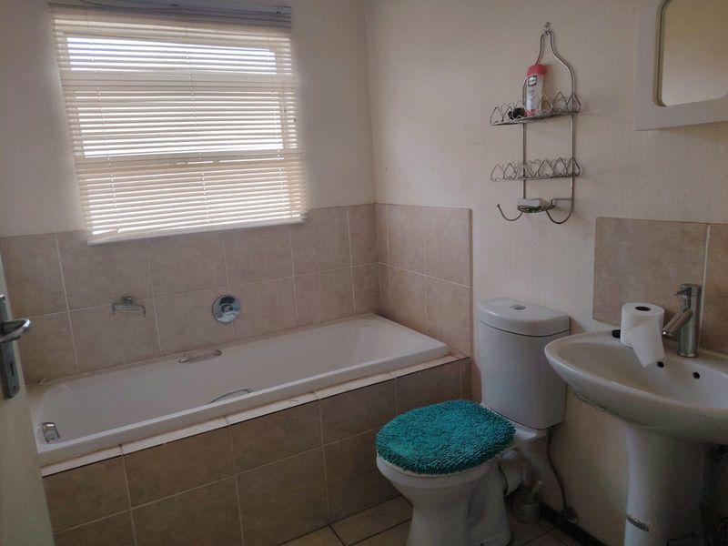 A functional bathroom featuring a built-in bathtub with tiled surround, a pedestal basin, and a standard toilet, finished with neutral wall tiles.