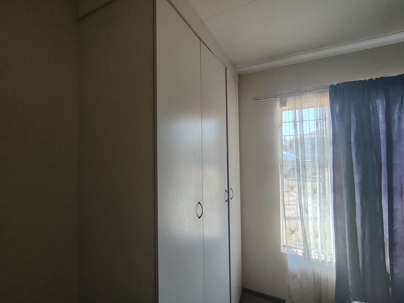 A bedroom featuring built-in cupboards and a window fitted with security bars.
