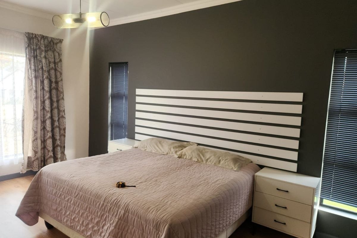 A well-maintained bedroom featuring laminate flooring, dark accent wall, built-in headboard, and modern venetian blinds.