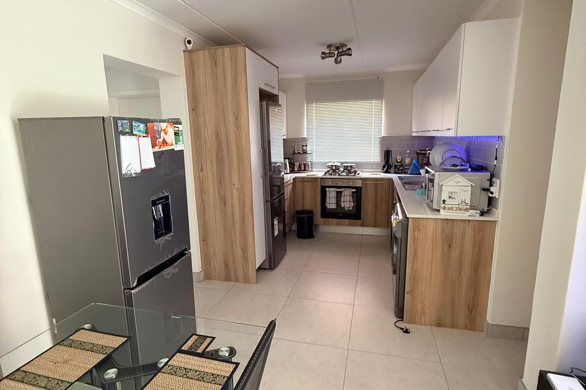 A functional kitchen featuring modern wood-look and white cabinetry, tiled flooring, and integrated appliances, offering a clean and practical cooking space.