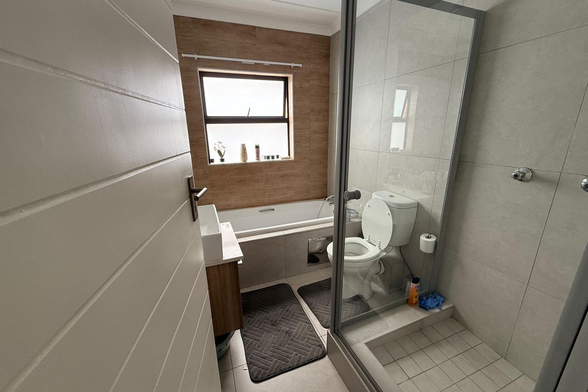 Modern bathroom featuring a glass-enclosed shower, a bathtub with wood-look tile surround, a vanity basin, and neutral floor-to-ceiling tiling.
