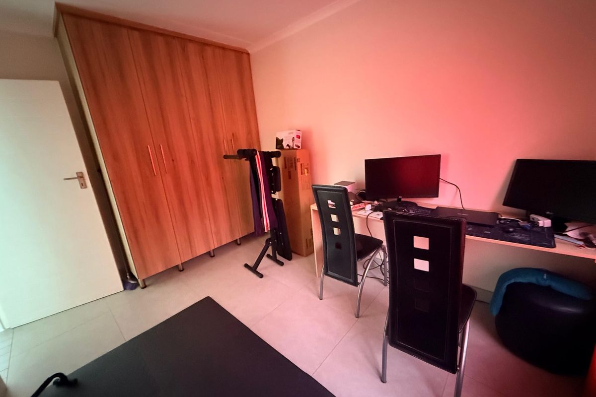 A bedroom featuring tiled flooring and a large built-in wooden wardrobe, currently utilized as a home office space.