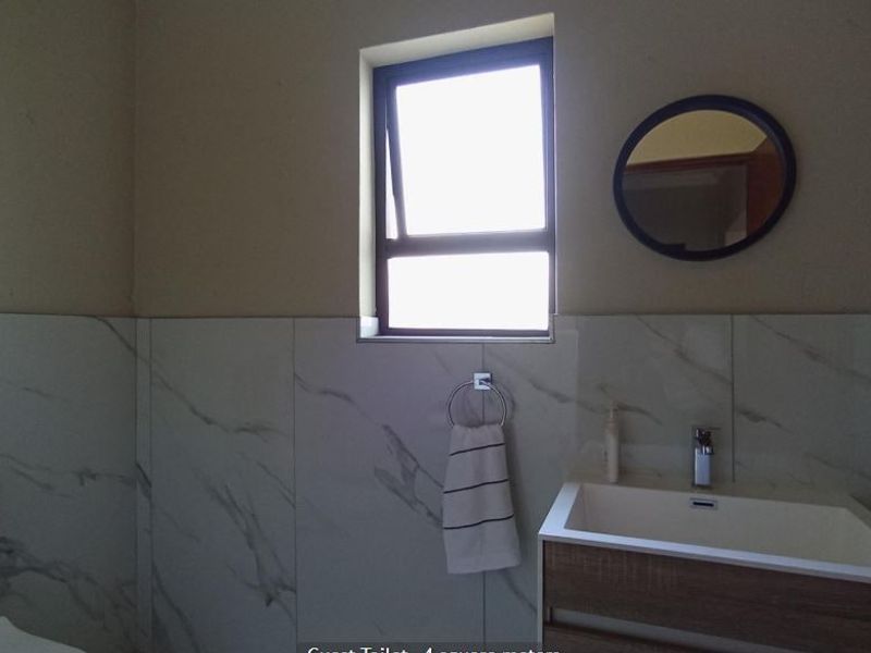 A functional guest bathroom featuring a modern vanity with basin, toilet, and marble-look wall tiling.