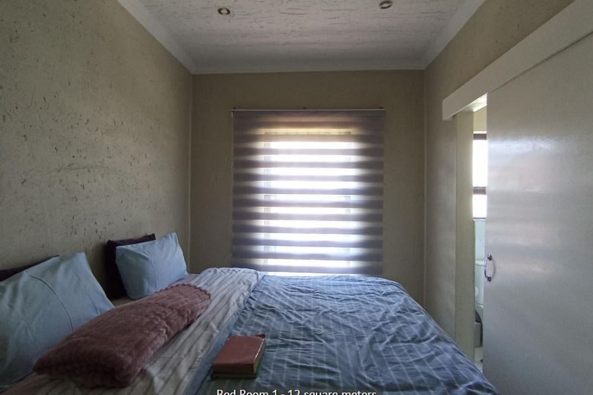 A bedroom featuring recessed ceiling lighting, a sliding door, and a roller blind, with visible wear on the wall finishes.
