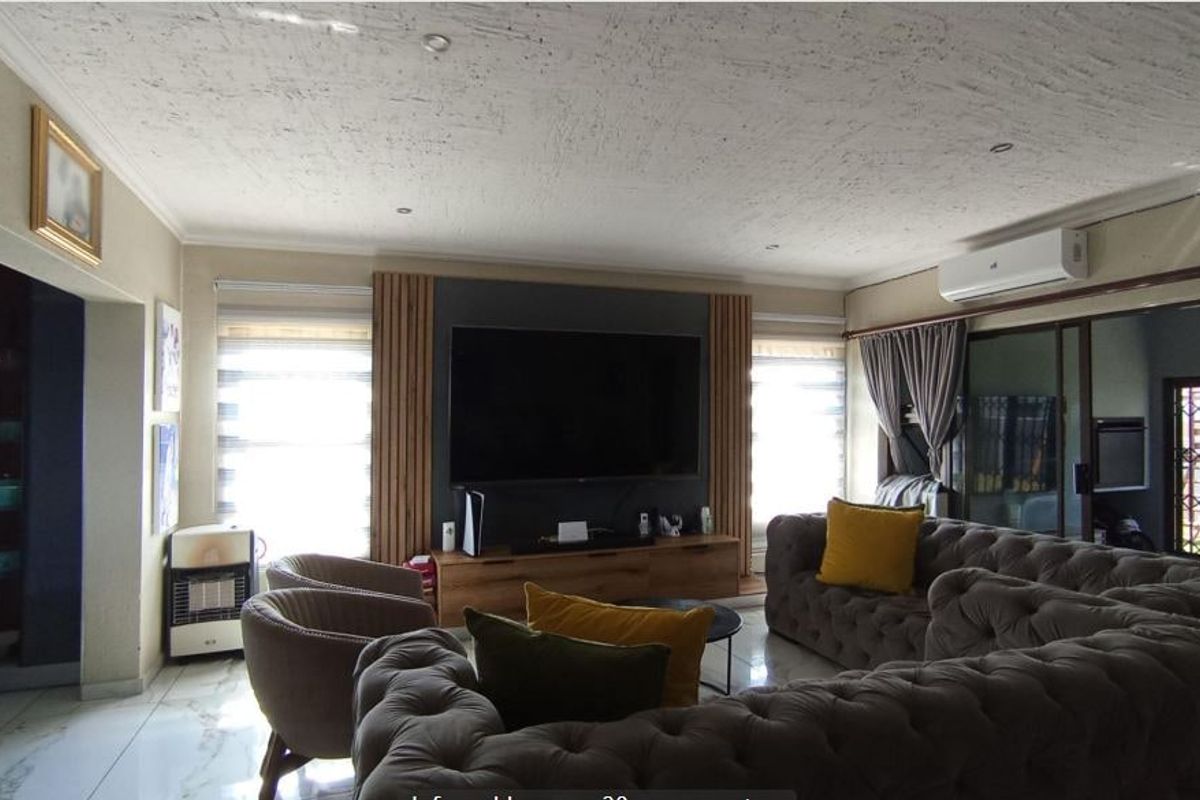 A well-maintained living room featuring modern wall paneling, tiled flooring, recessed lighting, and a split-system air conditioner.