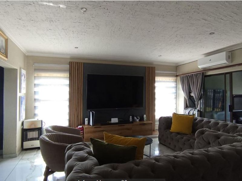 A well-maintained living room featuring modern wall paneling, tiled flooring, recessed lighting, and a split-system air conditioner.