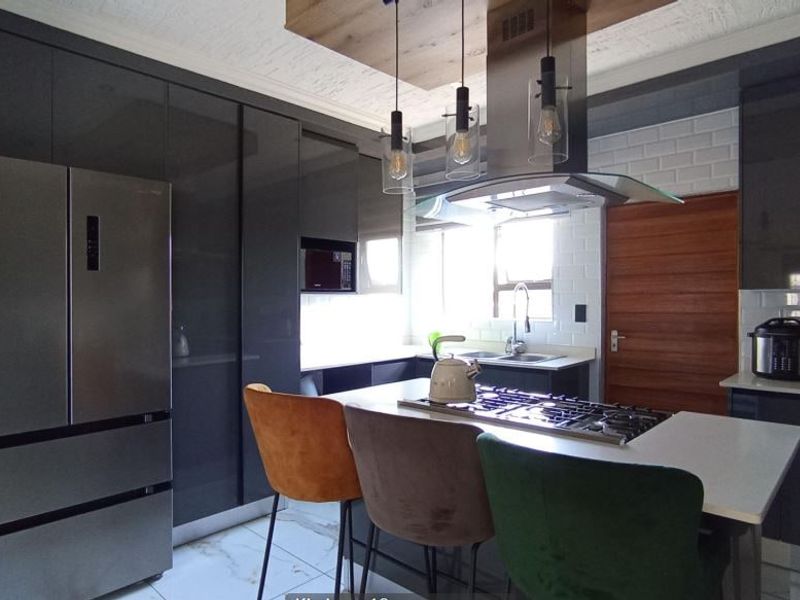 Modern kitchen featuring high-gloss cabinetry, a central island with a gas hob, subway tile backsplash, and contemporary pendant lighting.