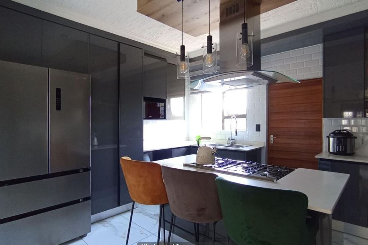 Modern kitchen featuring high-gloss cabinetry, a central island with a gas hob, subway tile backsplash, and contemporary pendant lighting.