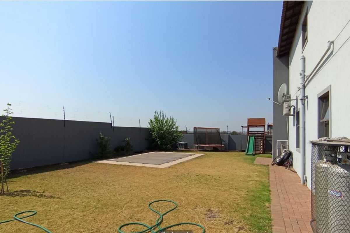 Rear garden area featuring a lawn, paved walkway, perimeter wall with electric fencing, and a covered swimming pool.