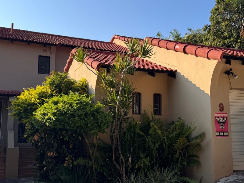 Front elevation of a townhouse featuring terracotta roof tiles, a paved driveway, and established garden landscaping.