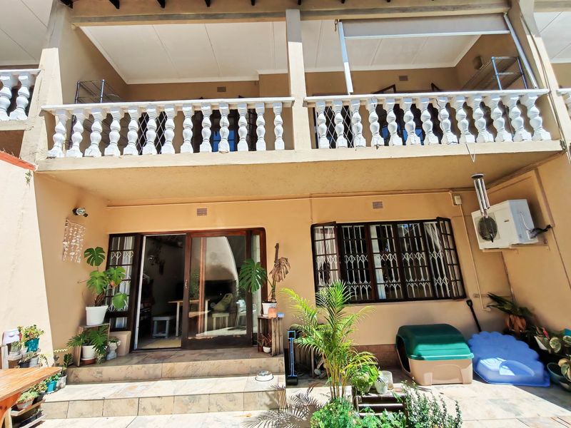 Rear view of a townhouse featuring a ground-level tiled patio, upper-level balcony with balustrade, and security-fitted windows and doors.
