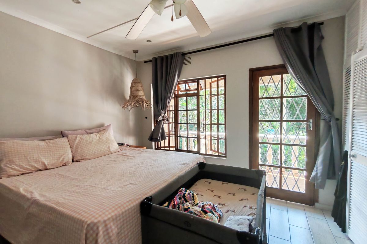A well-lit bedroom featuring tiled flooring, a ceiling fan, and direct access to an outdoor balcony through a wooden framed glass door.