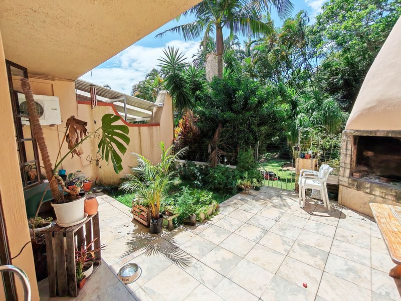 Covered patio area featuring a built-in braai, tiled flooring, and direct access to a lush, landscaped garden.