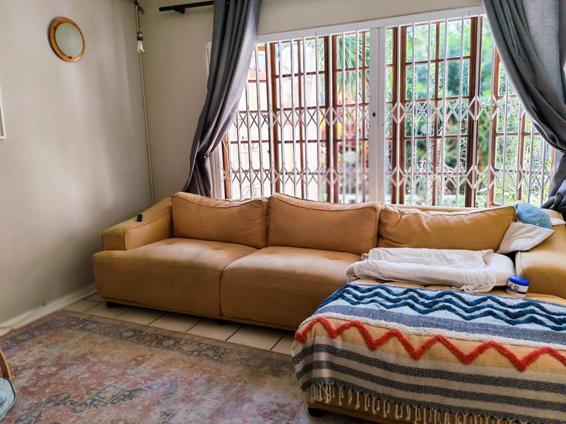 A living room area featuring tiled flooring and a large window fitted with a security gate and curtain rod.