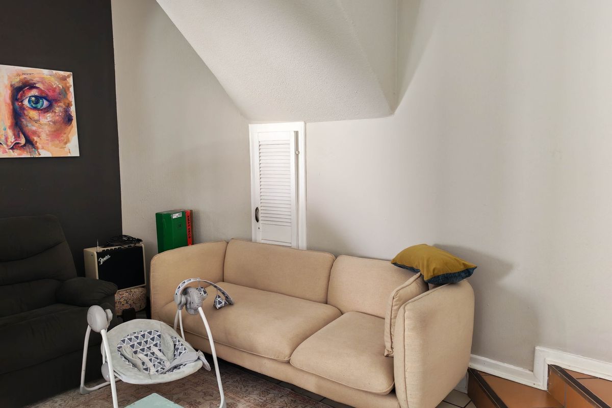 A living room area featuring a louvered storage cupboard and tiled staircase, with neutral wall finishes and a dark accent wall.