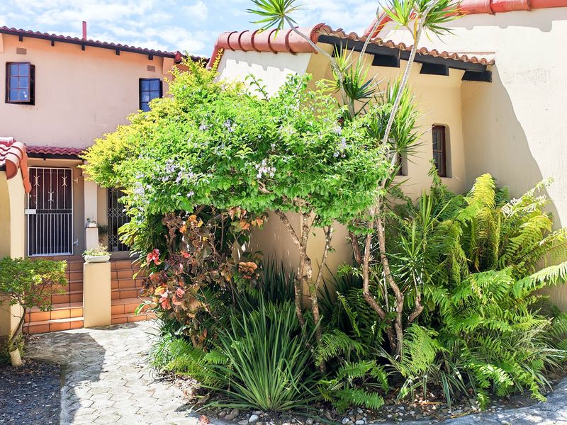 Front entrance of the townhouse featuring a paved walkway, terracotta steps, security gate, and established garden landscaping.