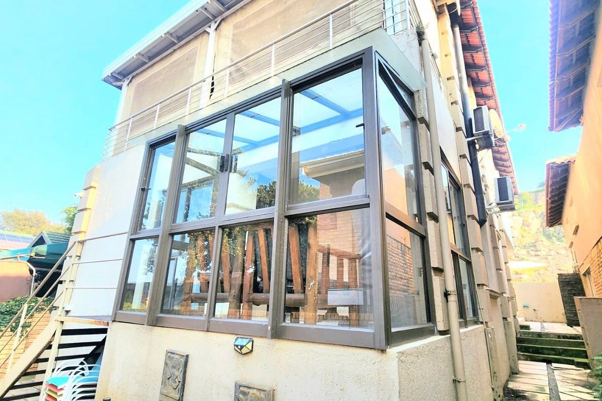 Rear view of the property featuring a glass-enclosed sunroom, metal balcony railing, and stone pathway leading along the side of the house.