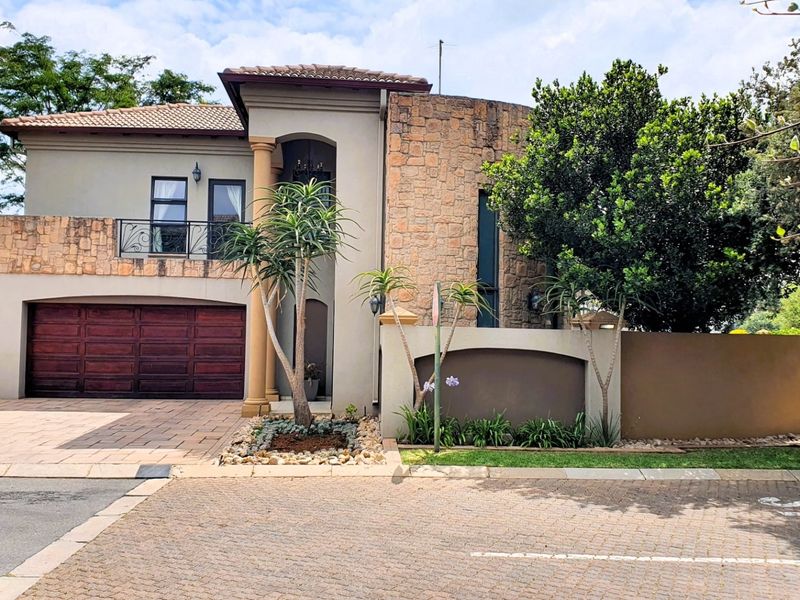 A well-maintained double-story residential home featuring stone cladding, a paved driveway, a double garage, and a balcony with wrought iron railings.