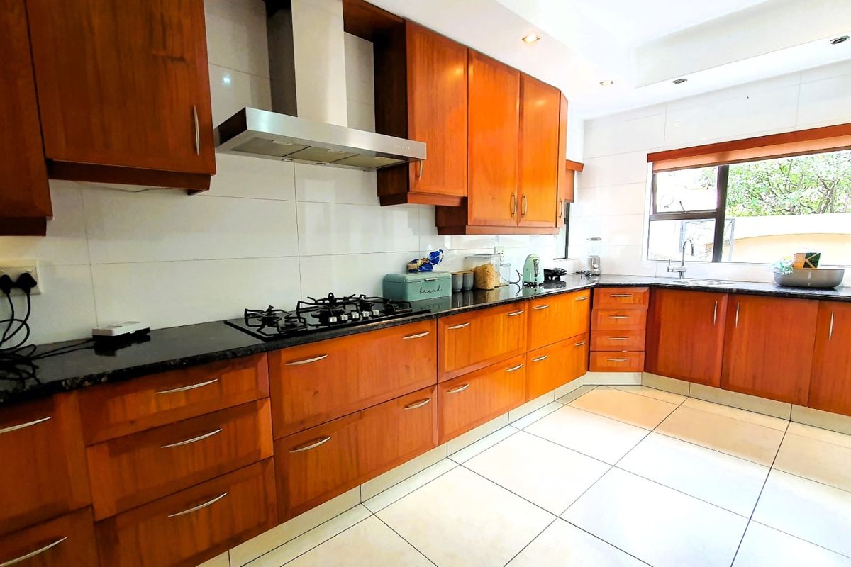A well-maintained kitchen featuring warm wooden cabinetry, granite countertops, a gas hob with an extractor fan, and neutral tiled flooring.