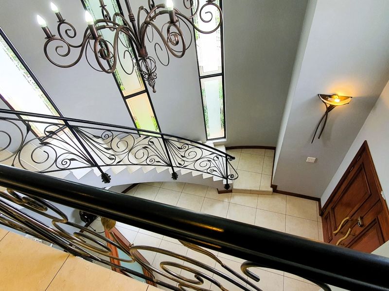 A grand entrance hallway featuring a sweeping staircase with ornate wrought iron railings, tiled flooring, and elegant lighting fixtures.