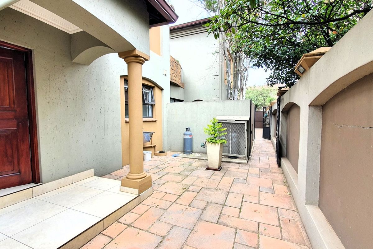 A paved rear patio area featuring a covered entrance, decorative column, and high boundary walls, providing a private outdoor space.