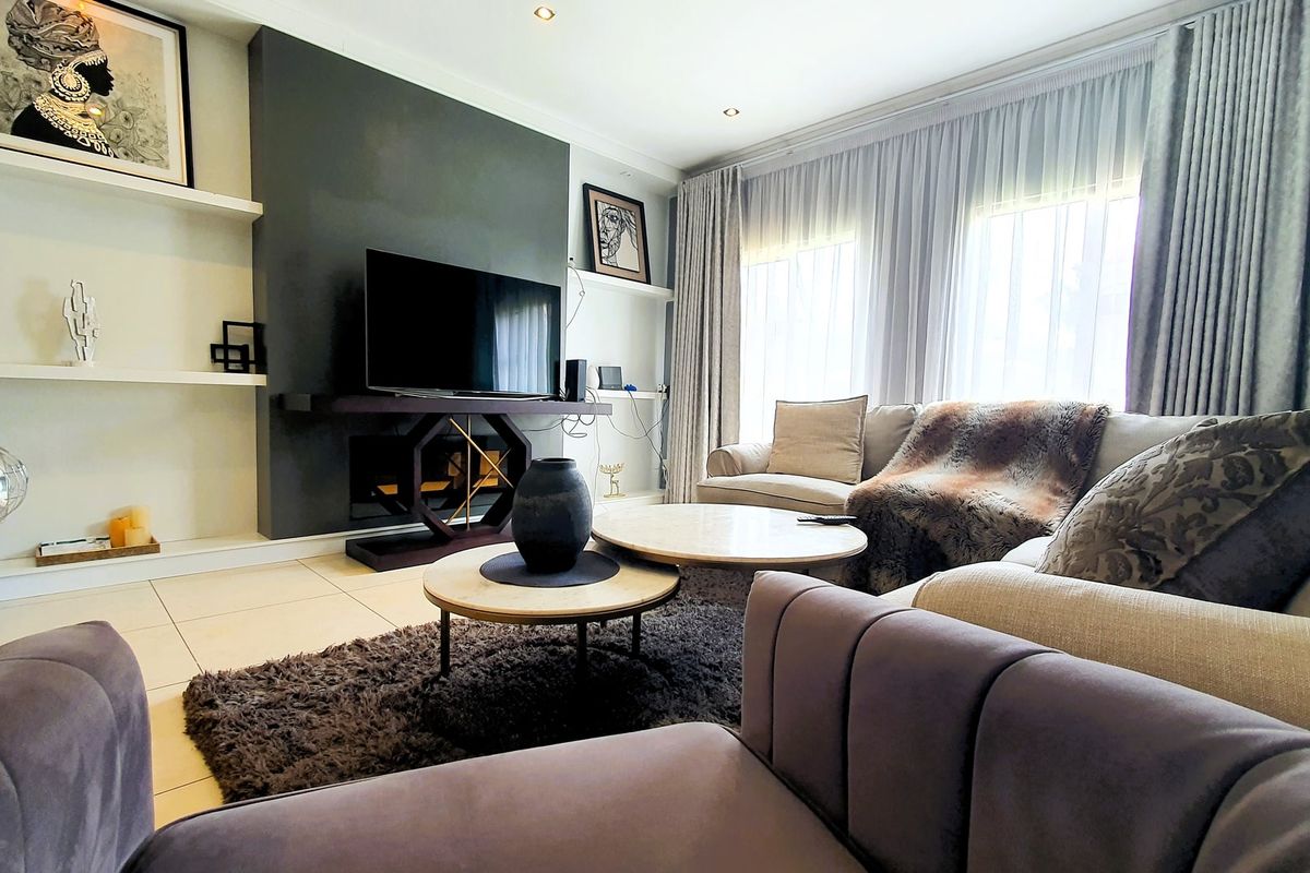 A well-maintained living room featuring a modern dark feature wall, built-in shelving, tiled flooring, and recessed downlighting with ample natural light.