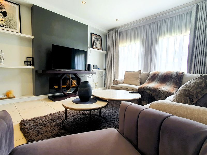 A well-maintained living room featuring a modern dark feature wall, built-in shelving, tiled flooring, and recessed downlighting with ample natural light.