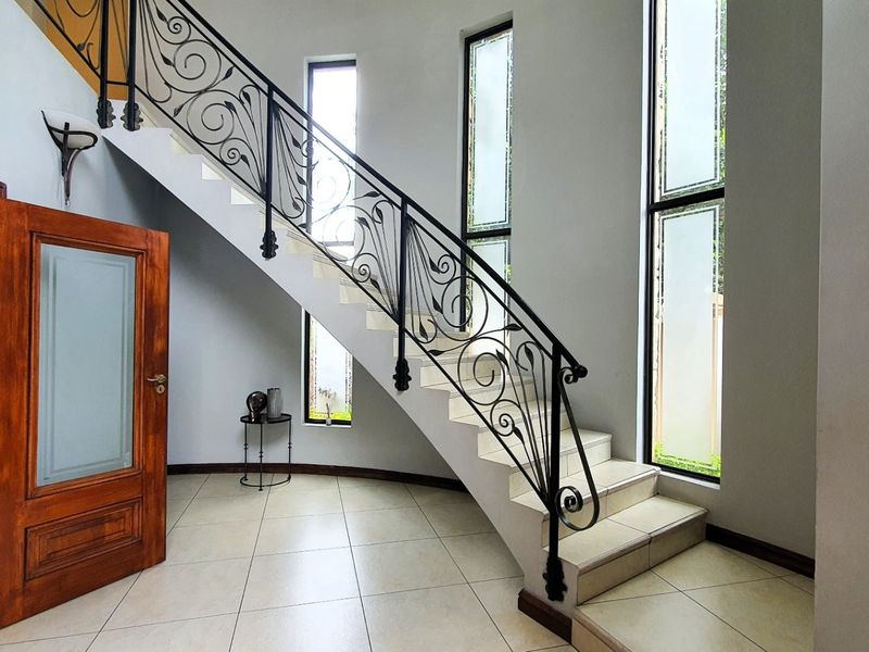 Bright entrance foyer featuring a striking wrought iron staircase railing, tiled flooring, and tall vertical windows that provide ample natural light.